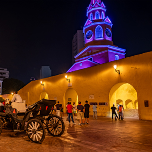 Perspectiva nocturna de la Torre del Reloj con sus tradicionales coches de caballos, donde la luz cálida refuerza la monumentalidad de este emblemático acceso a la Ciudad Amurallada.