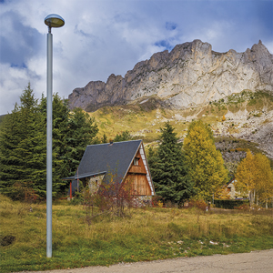 Panoramic view with imposing mountains and a pitched-roof building, with a Metrópoli LP luminaire in the foreground.